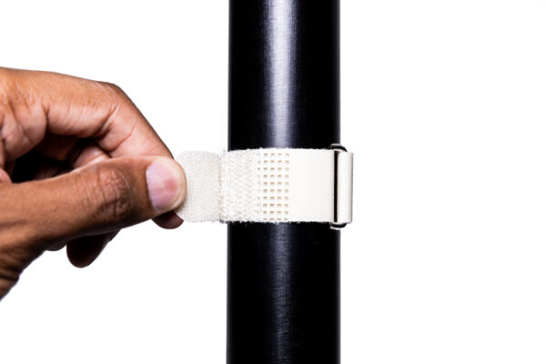 IMG_0064 - Speedtech International A hand secures a SPEEDWRAP® High Temp Cinch Strap around a black cylindrical pole against a white background.