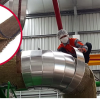A worker in safety gear wraps VELCRO® Brand HI-GARDE® Fasteners around a large industrial pipe; an inset shows a close-up of the brown, fibrous fastener. The factory setting features metal pipes and a metal roof.